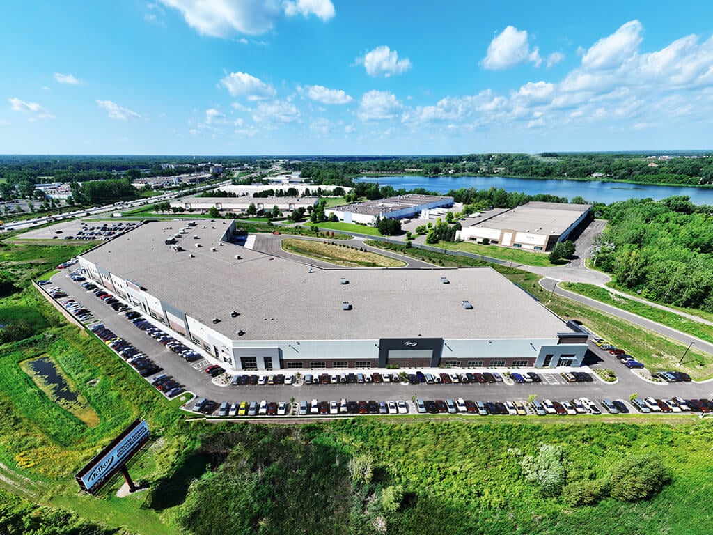 A birds eye view of Delkor's manufacturing campus shows four large buildings with bright green grass and a blue sky with a few clouds