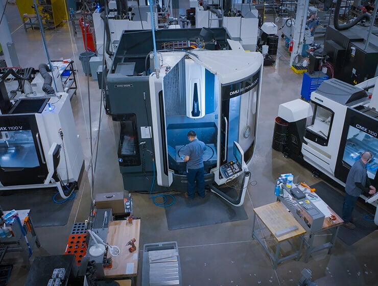 A birds eye view of Delkor's advanced machining center. A production floor with multiple machines and a few employees working.